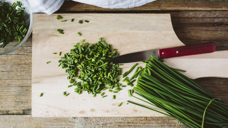 Chopped and whole chives on wooden cutting board