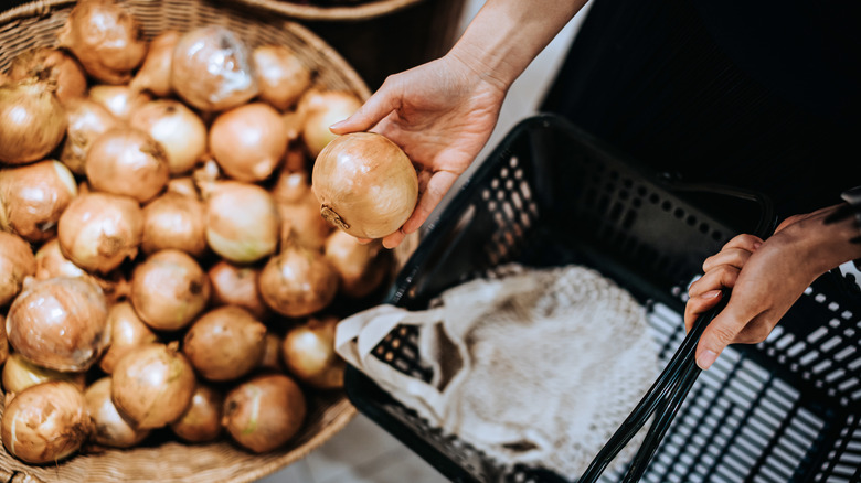 hand putting onions in basket at store