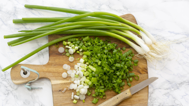 chopped and whole scallions on wooden cutting board