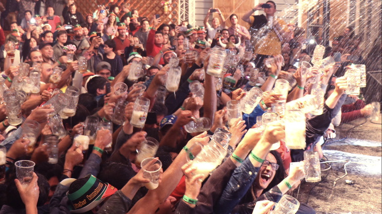 Crowd of people try to catch spray of beer in their glasses