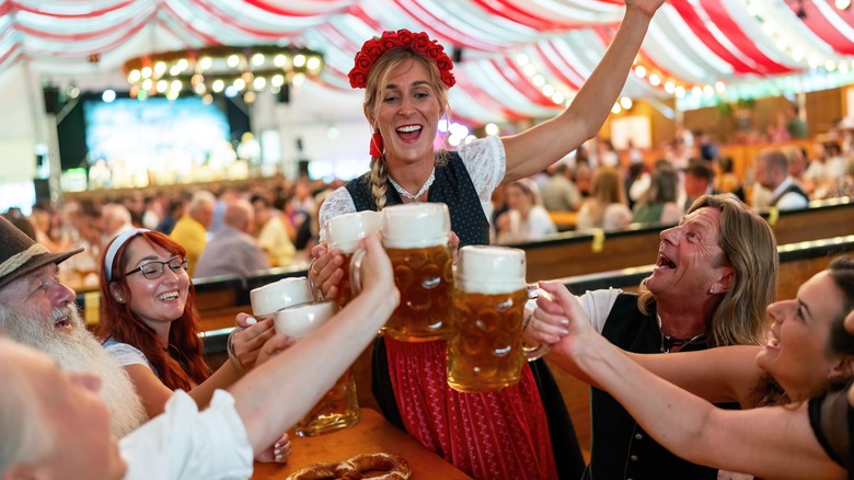 Group of smiling adults in Bavarian attire clink beer glasses