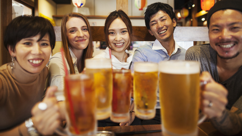 Smiling group of people extend glasses of beer together