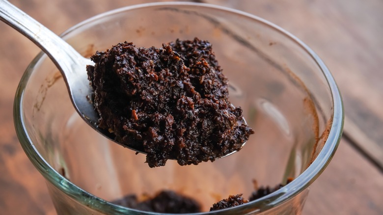 Spoon scooping used coffee grounds out of a glass mug