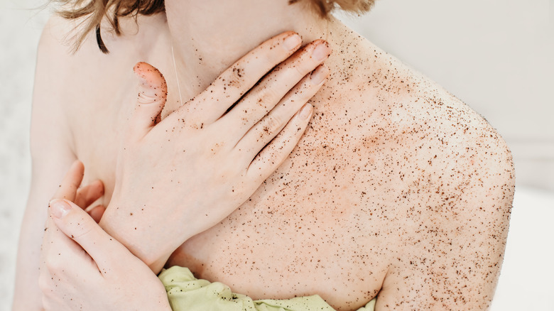 Woman in towel applying coffee body scrub to her arms and chest