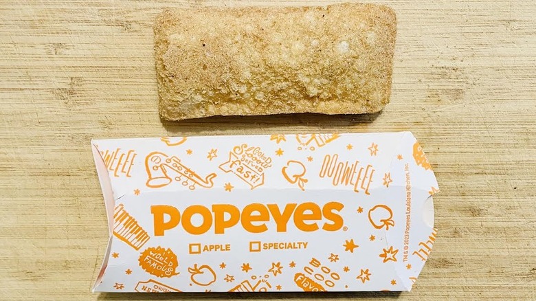 Popeyes Cinnamon Apple Pie next to paper sleeve packaging