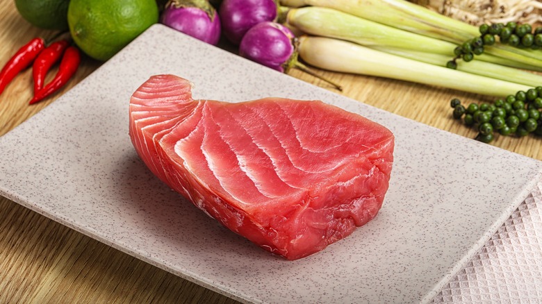 A raw tuna steak on a gray plate with vegetables surrounding it