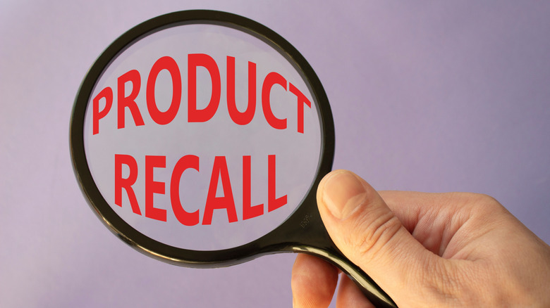 Hand holding a magnifying glass with the words "Product Recall" inside