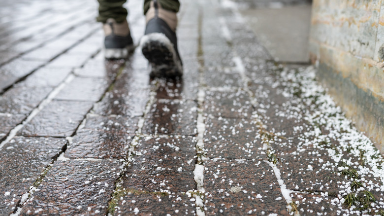 Salt grains on icy sidewalk with person walking away in winter boots