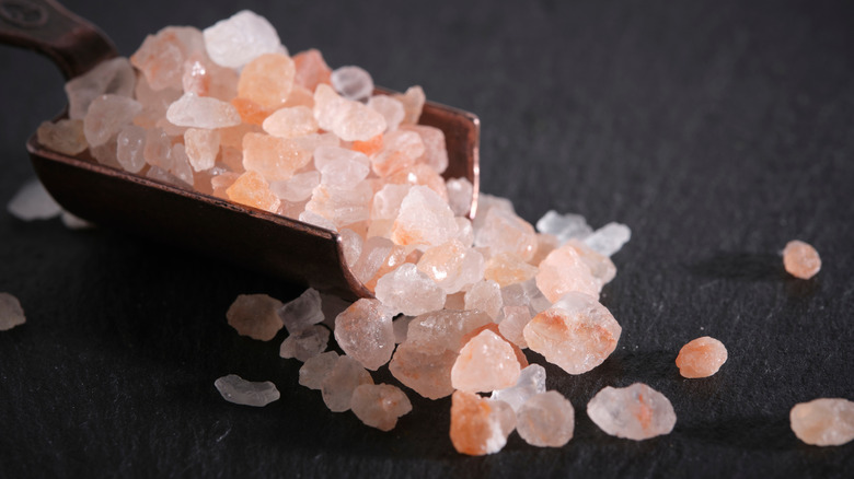 Metal scoop filled with large pink salt crystals on black table