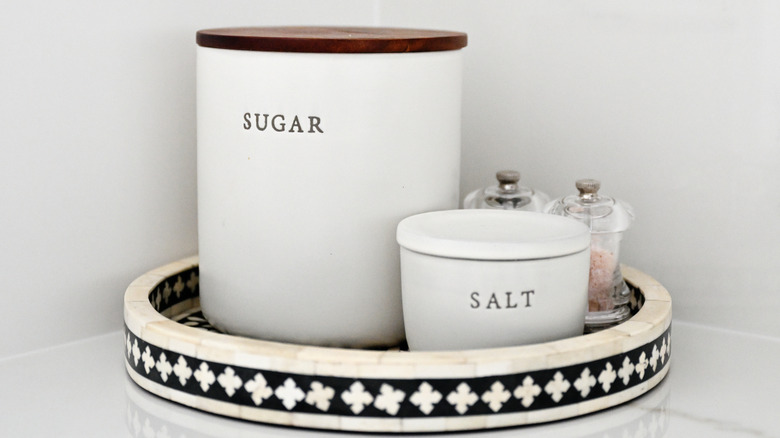 White canisters with labels for sugar and salt on black and ivory tray