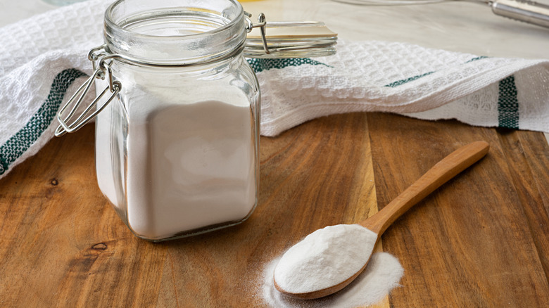 baking soda on a wooden spoon next to a glass jar.