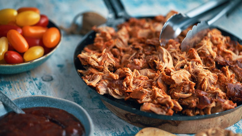 skillet of pulled chicken with tongs