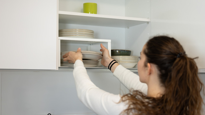 Woman storing dishes in kitchen cabinet with organizer shelf