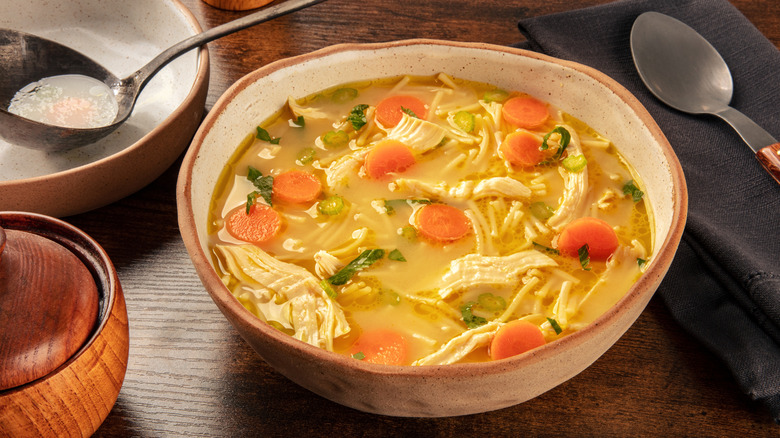 chicken noodle soup in a beige bowl next to a spoon.