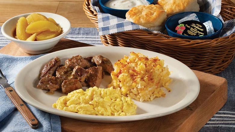 scrambled eggs, steak, and hashbrowns on a plate next to a basket of biscuits