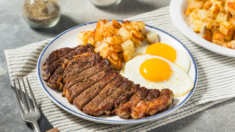 New York strip steak, hasbrowns, and eggs on a white plate