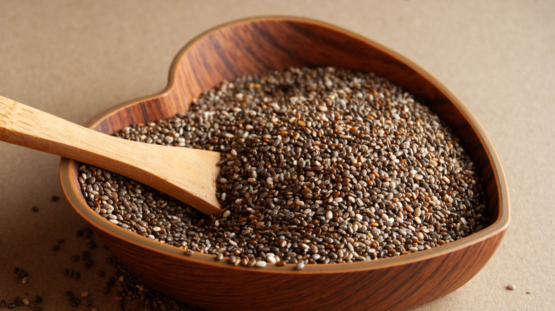 Chia seeds in a heart-shaped wooden bowl with a wooden spoon.