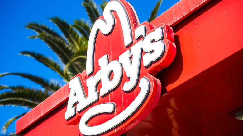Close-up view of the iconic red Arby's logo sign against a bright blue sky.