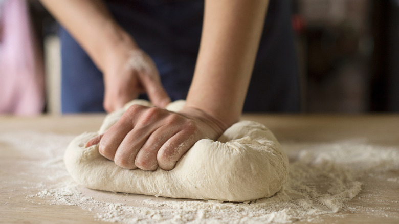 Hands kneading dough on floured surface
