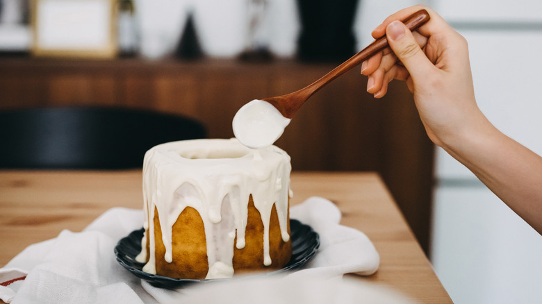 Hand holds wooden spoon pouring icing onto cake