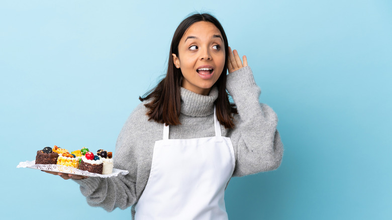 Woman holding plate of small cakes with her hand to her ear