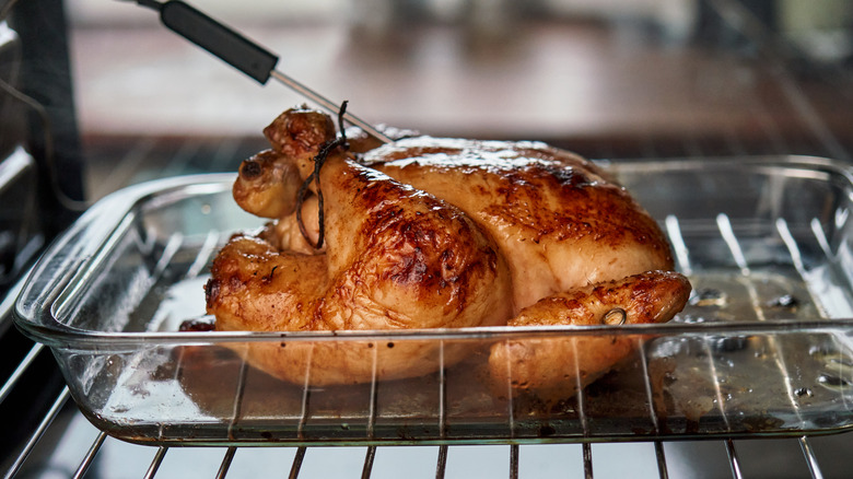 A chicken roasting in a glass dish with a probe thermometer