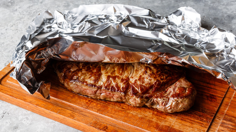 A steak resting on a cutting board partially covered