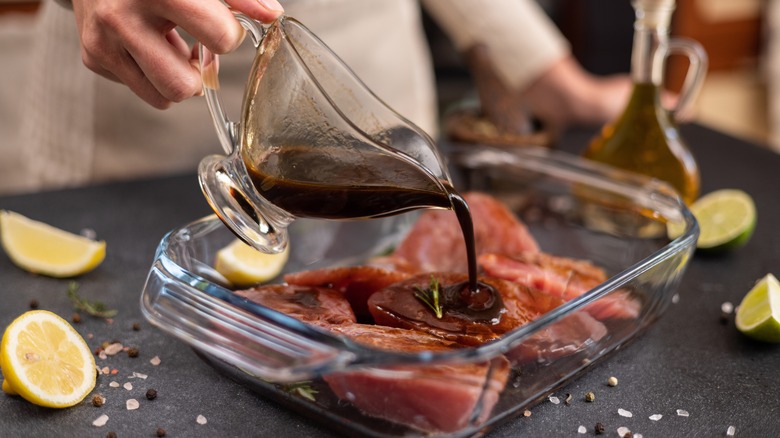 Person pouring soy sauce marinade over meat