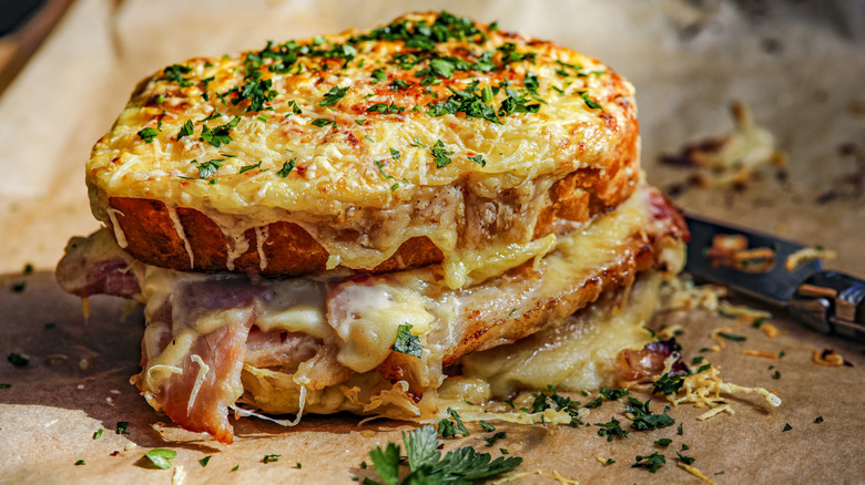 A toasted croque monsieur with melted cheese and herbs sprinkled on top