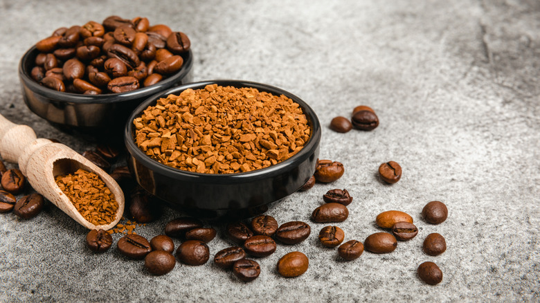 A black bowl with coffee beans and a black bowl and wooden spoon holding instant coffee granules