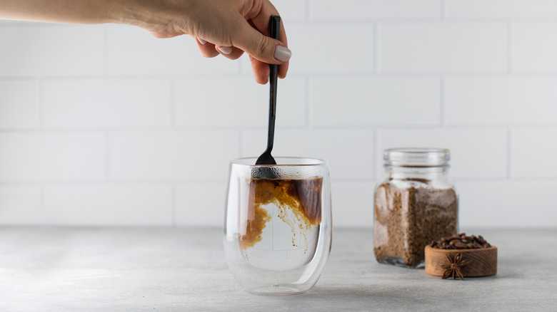 A hand stirring a spoon instant coffee in a glass with hot water