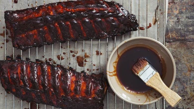 Brushing sauce on charred ribs on a grill grate