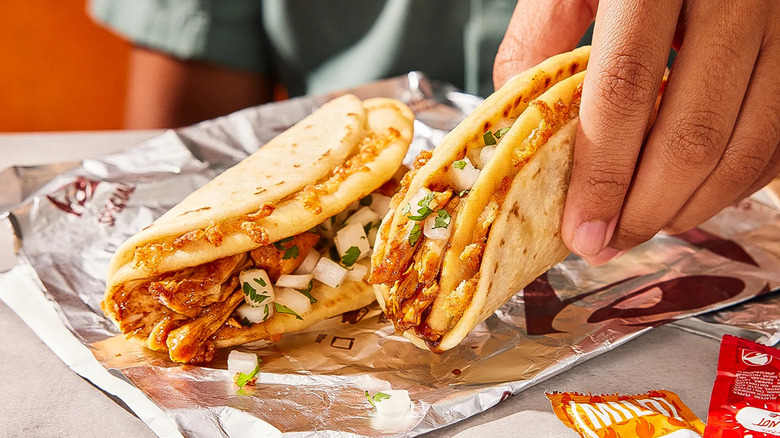 A hand picks up a Cheesy Street Chalupa that was on a wrapper.