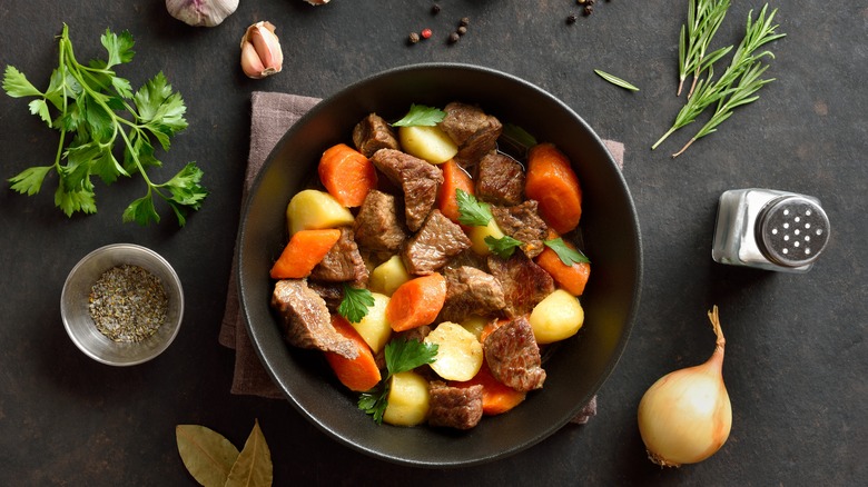 A bowl of beef stew surrounded by ingredients