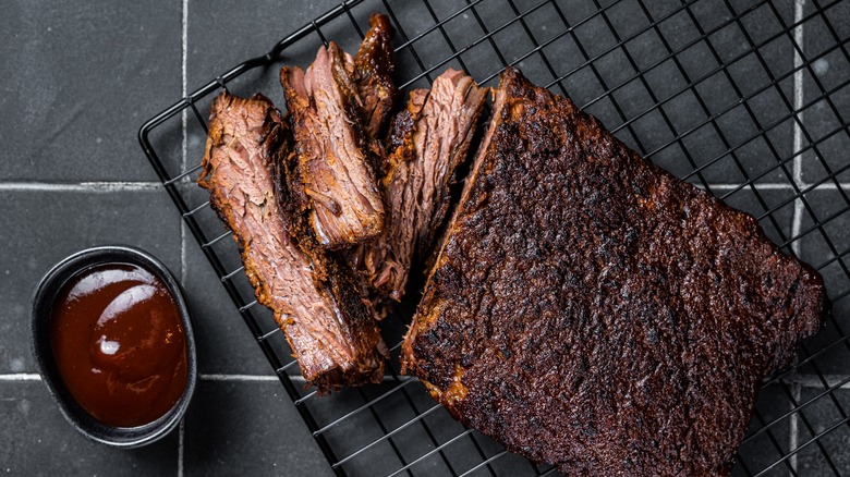 Smoked brisket on a wire rack next to a cup of sauce