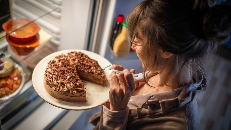 woman holding plate of cake near refrigerator