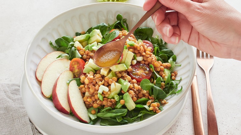 spoon with dressing being held over a salad