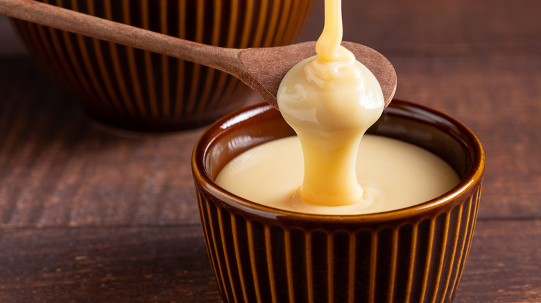 Wooden spoon drizzling sweetened condensed milk into a bowl