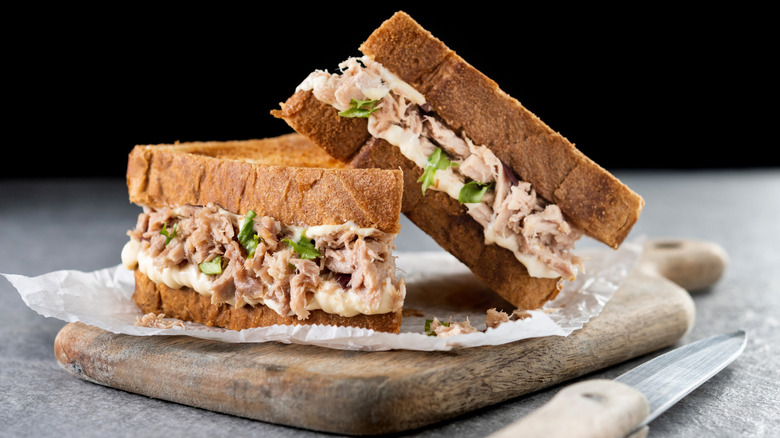 Two halves of a tuna sandwich sitting on wax paper on top of a cutting board,