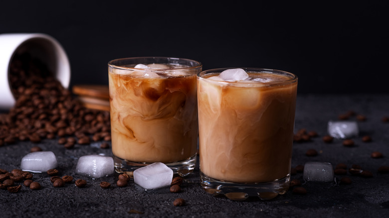 Two small galsses of iced cafe lattes on a black table