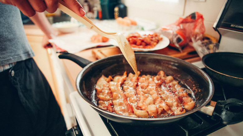 A person fries bacon on the stove