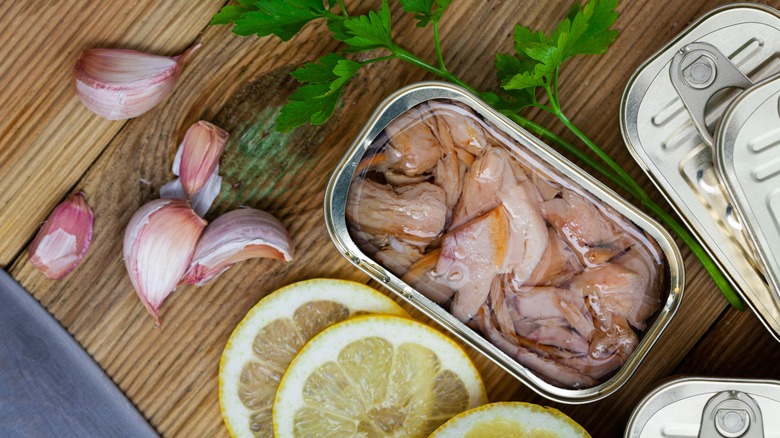 Open can of tuna next to garlic cloves and lemons