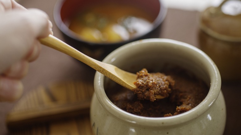 Scooping miso paste out of a jar with a wooden spoon