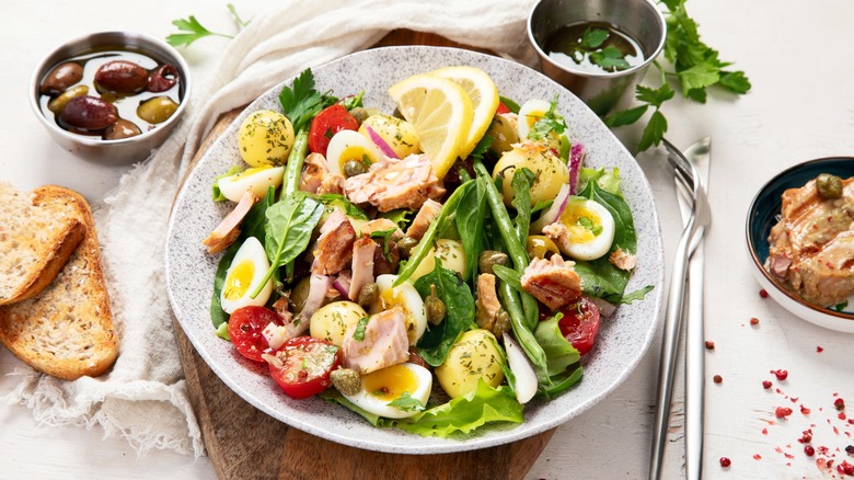 Bowl of nicoise salad, cutlery, bread, and olives