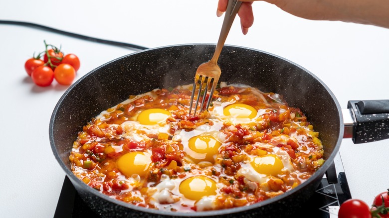 hand stirring eggs in shakshuka
