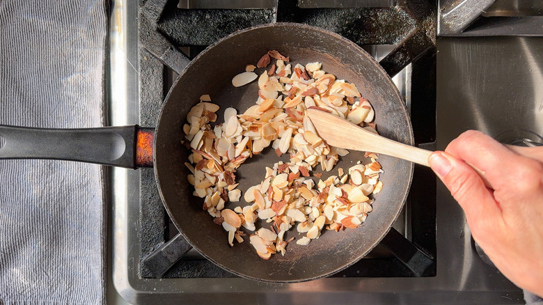 Stirring slivered almonds in skillet on stovetop with wooden spoon