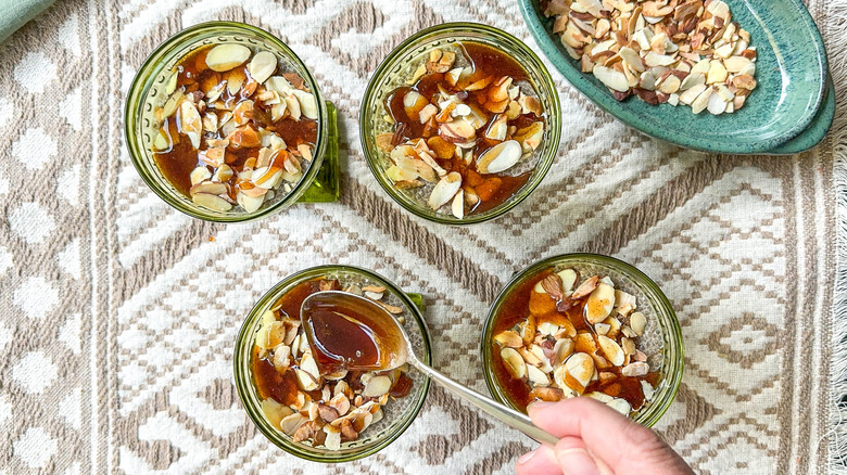 Drizzling chai maple syrup over almonds on chai chia puddings in serving dishes