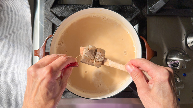 Removing chai tea bags from almond milk in pot on stovetop using wooden spoon