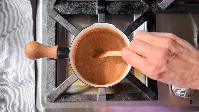 Stirring maple chai syrup in small saucepot on stovetop with wooden spoon