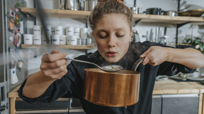 woman tasting food from saucepan